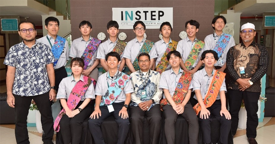 「INSTEP」と書かれた看板を背景に、伝統的なバティック柄のたすきを身につけた人々がロビーに立ったり座ったりしている群像。(写真)